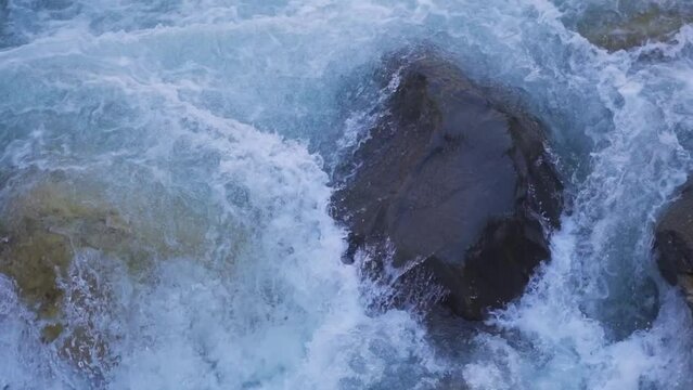 Closeup slow motion shot of a rock obstructing the flow of the river Parvati at Kasol in Himachal Pradesh, India. Natural background. Rock in river stream . Natural forest background. 