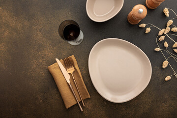 Table setting, empty plate with napkin and cutlery on a brown background, top view of the served table decorated with dry flowers
