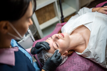 Permanent makeup artist prepares the client's face with the procedure, cleans the eyebrows from...