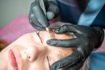 Procedure of eyebrow microblading. A master in black gloves is doing a blending needle of model's brow.