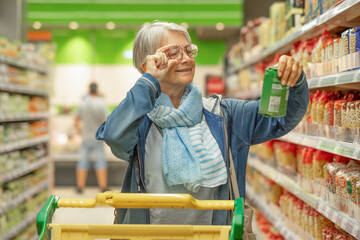 Portrait smiling senior woman making purchases in the supermarket selecting checking a product....