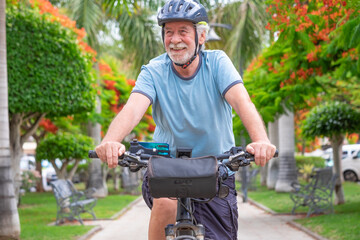 Happy active senior man cycling in the public park with electric bicycle enjoying freedom. Concept of healthy lifestyle and sustainable mobility