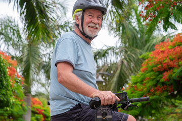 Happy active senior man cycling in the public park with electric bicycle looking back. Concept of healthy lifestyle and sustainable mobility