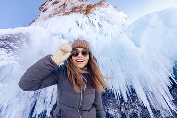 Happy young woman tourist in sunglasses on background ice cave grotto, frozen waterfall or lake...