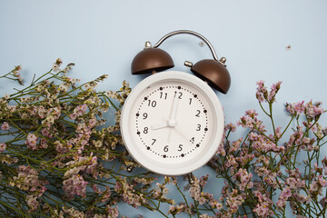 Alarm clock and flowers with space copy on blue background