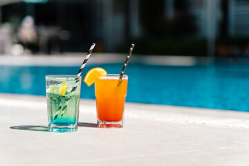 Tropical sparkling lemonade cocktails by the pool. Glasses with orange and mint lemon fruit cocktails. Summer alcohol free drink by the hotel pool. Hello summer holiday vacation