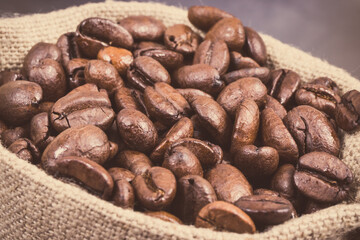 Heap of dark roasted coffee grains in jute bag. Vintage photo