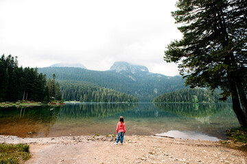 Little toddler girl stands and looks at Black Lake, Crno jezero, Durmitor, Montenegro. Nature and people. Wide angle. Alone, loneliness