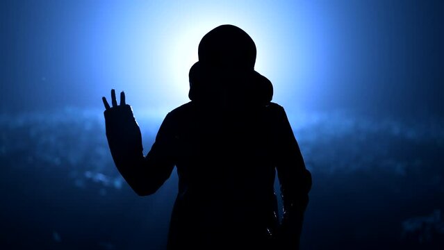 Silhouette of alien waving hand - hello on blue, night background. Humanoid on extraterrestrial planet. UFO, fantasy, futuristic, fiction concept.