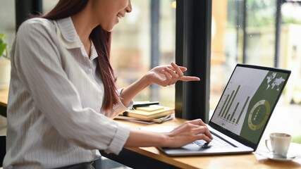 Young female investor analyzing stock charts on laptop screen, sitting in modern coffee shop