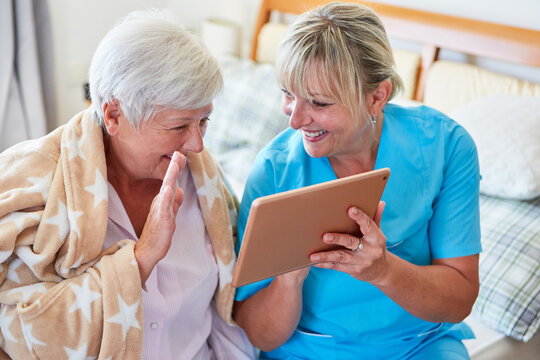 Geriatric nurse supports happy elderly woman with video chat