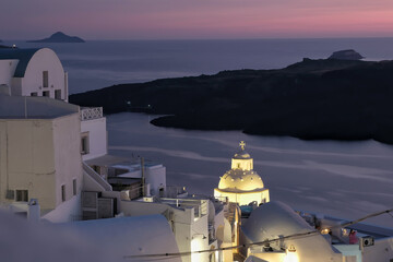 View of the illuminated picturesque village of Fira Santorini, the volcano and a beautiful purple...