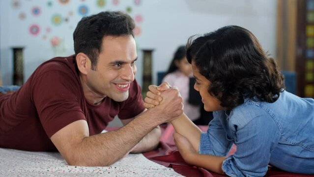 A young boy playing arm-wrestling with his father - physical strength happy parenting a competitive match. A happy Indian family together at home - family bonding leisure time an Indian house...