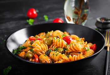 Classic italian pasta fusilli marinara with mussels, green olives and capers on dark table. ...