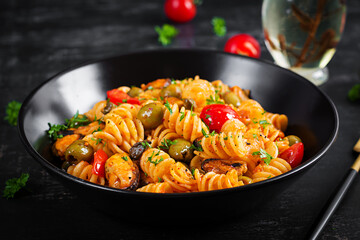 Classic italian pasta fusilli marinara with mussels, green olives and capers on dark table. ...
