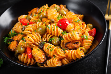 Classic italian pasta fusilli marinara with mussels, green olives and capers on dark table.  Fusilli pasta with sauce marinara