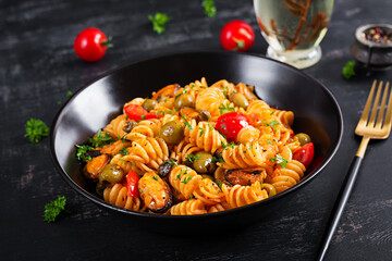 Classic italian pasta fusilli marinara with mussels, green olives and capers on dark table.  Fusilli pasta with sauce marinara