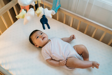 adorable asian newborn child is looking upward at the colorful hanging toys with curiosity while...
