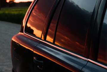 SUV on off-road rocky road. A beautiful red summer evening sunset is reflected in the SUV's tinted...
