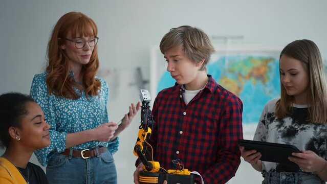 Cheerful students showing their builded robotic toy to young science teacher at robotics classroom at school.