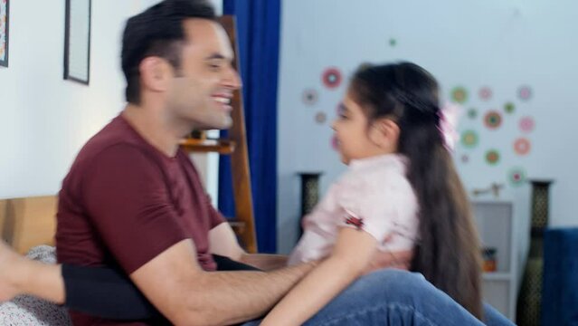 An Indian beautiful little girl sitting on her father's lap and playing with him - togetherness and bonding  Bedtime play. A cheerful Indian father spending quality time with his little daughter - ...