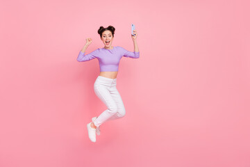 Fototapeta na wymiar Full length body size view of attractive cheery trendy girl jumping using device rejoicing isolated over pink pastel color background