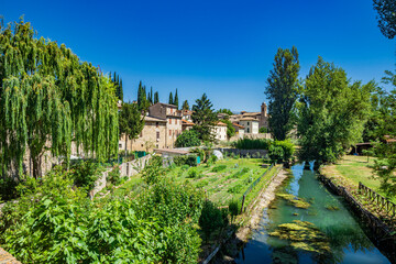Fototapeta na wymiar The Chiasco river that crosses the ancient medieval village of Bevagna. Perugia, Umbria, Italy. Trees, vegetation, cultivated gardens. Green algae on the surface of the stagnant water.