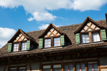 Fototapeta na wymiar Old vintage European decorated attic windows with open wooden shutter and facade decoration in a small village in Switzerland. Cloudy blue sky in the background, no people