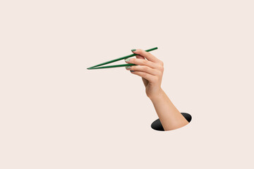 Female hand holding green chopsticks on clean pink background - obrazy, fototapety, plakaty