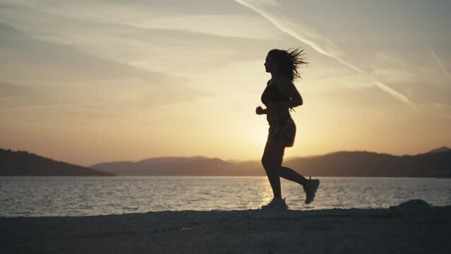 Time-lapse video of a girl jogging by the sea at sunset. Active lifestyle workout at sunrise in beautiful ocean scenery. High quality 4k footage