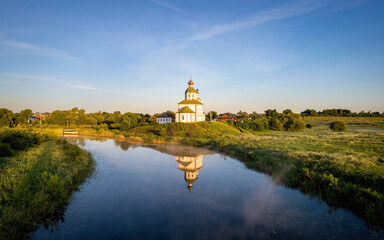 Fototapeta na wymiar Small christian church on the river on a sunrise (aerial drone photo). Suzdal, Russia