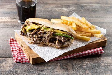 Philly cheesesteak sandwich with beef, cheese,green pepers and caramelized onion on wooden table