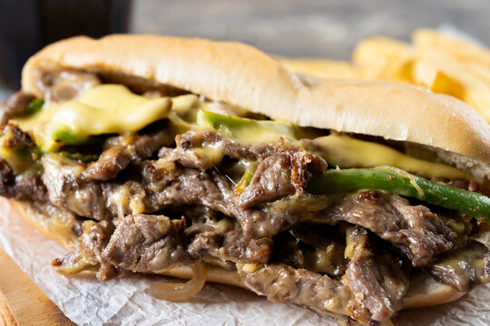 Philly cheesesteak sandwich with beef, cheese,green pepers and caramelized onion on wooden table