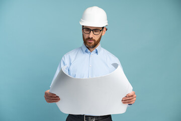 Architect man with concentrated face in builder safety helmet looking at the blueprints over...