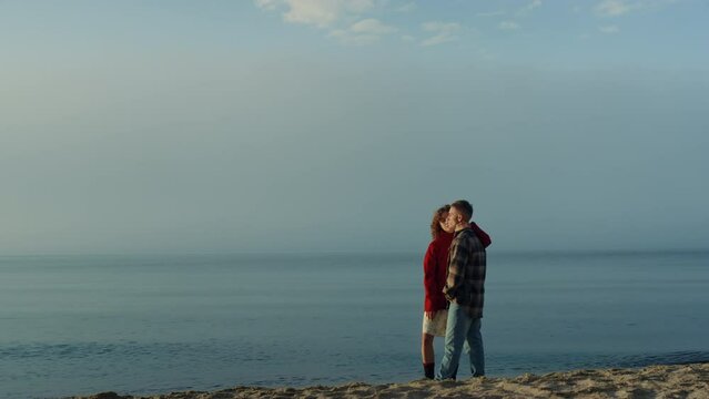 Affectionate couple standing on sea shore. Loving woman kissing man in cheek 
