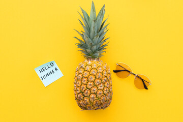 Funny pineapple with sunglasses and word hello summer on yellow background