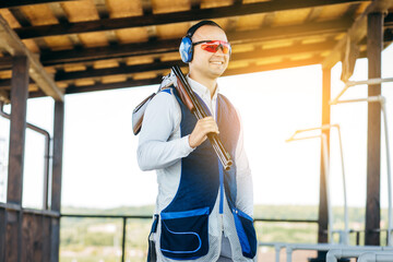 Portrait of adult man in sunglasses, protective headphones and a rifle vest practicing fire weapon...