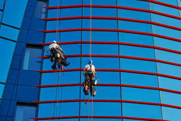 Two workers cleaning window in business center, Industrial alpinists washing exterior of...