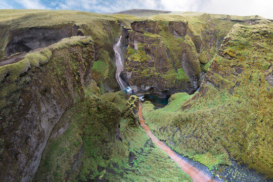 Waterfall meeting with brown stream in Fjaorargljufur Canyon with green flora and blue water in tranquility.in Iceland