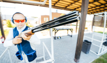 Blurred background with focus on front of shotgun barrel of adult man in sunglasses, protective...