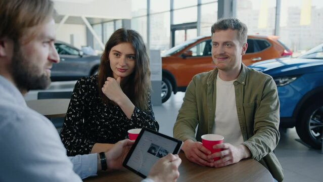 A dealership manager shows a young couple options for buying a new car on a tablet