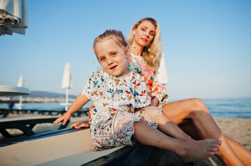 Fototapeta na wymiar Mother and beautiful daughter having fun on the beach, sitting on sunbed. Portrait of happy woman with cute little girl on vacation.