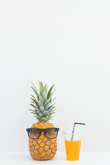 Fresh pineapple with sunglasses near a glass of juice and a cocktail straw on color background