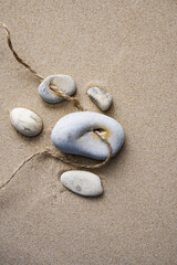 Fototapeta na wymiar Stone with natural hole on sand background. Adder stone, Hag stone or chicken god amulet on thread