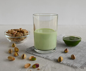 Pistachio milk in a glass, pistachio paste, and pistachio on a linen napkin. This milk is a great source of antioxidants, phytosterols, and heart healthy fats