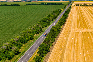 cargo delivery. trucks driving on asphalt road along the green fields whith rolls of haystacks.