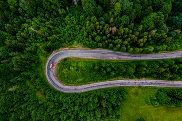 red car driving along the mountain asphalt road. road through beautiful green forest. seen from the air. Aerial top view landscape. drone photography. mountain serpentine