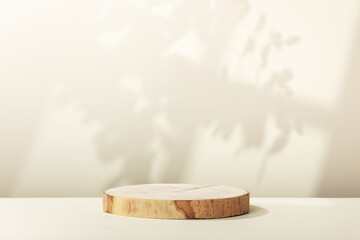 Wood slice podium with leaves  and window shadows on beige background for cosmetic product mockup - obrazy, fototapety, plakaty