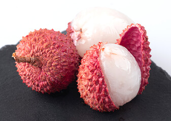 Lychee with peel and peeled lychee on a black board, isolated on a white background