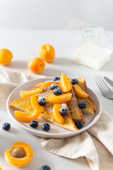Sweet french toast with berries and syrup served on plate. Copy space for text. Healthy breakfast: toasts with blueberry and apricots and milk on white background. Side view, close up.